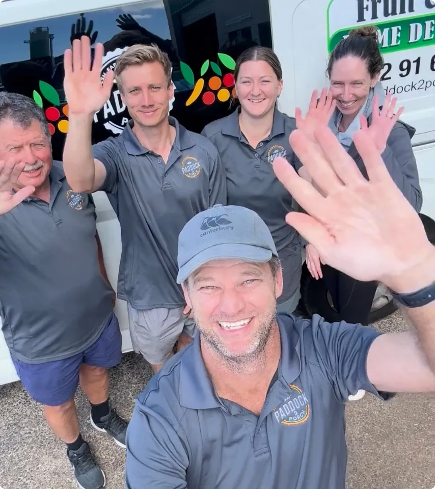 Five people wearing matching "Paddock" shirts stand outside and wave at the camera, smiling, in front of a white van with signage.